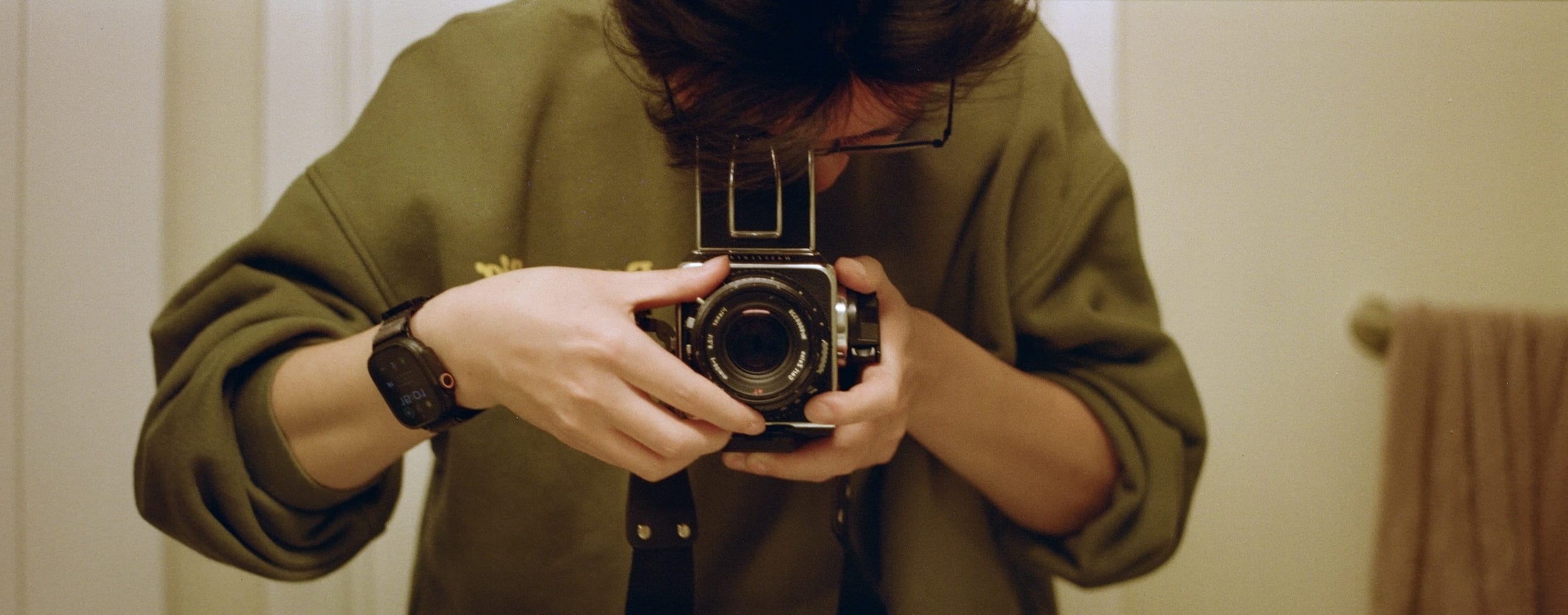 Mirror self-portrait on film — face hidden behind a Hasselblad
